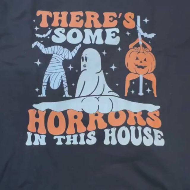 Video of a Black Gildan Ultra Cotton Halloween shirt with funny retro graphic of ghost, mummy, and pumpkin with text “There’s Some Horrors in This House"