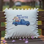 video of beige embroidered throw pillow with a vintage blue truck filled with spring flowers and the text 'Happy Easter' embroidered on it, surrounded by a pom-pom trim.