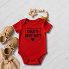 Red baby onesie with 'Dad's Best Gift' text on a light wooden floor.