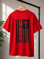 A red short-sleeve T-shirt hanging on a wooden hanger from a black clothing rack, featuring a large black distressed American flag-style graphic on the back with the word 'FAITH' running vertically and a red cross inside the flag.