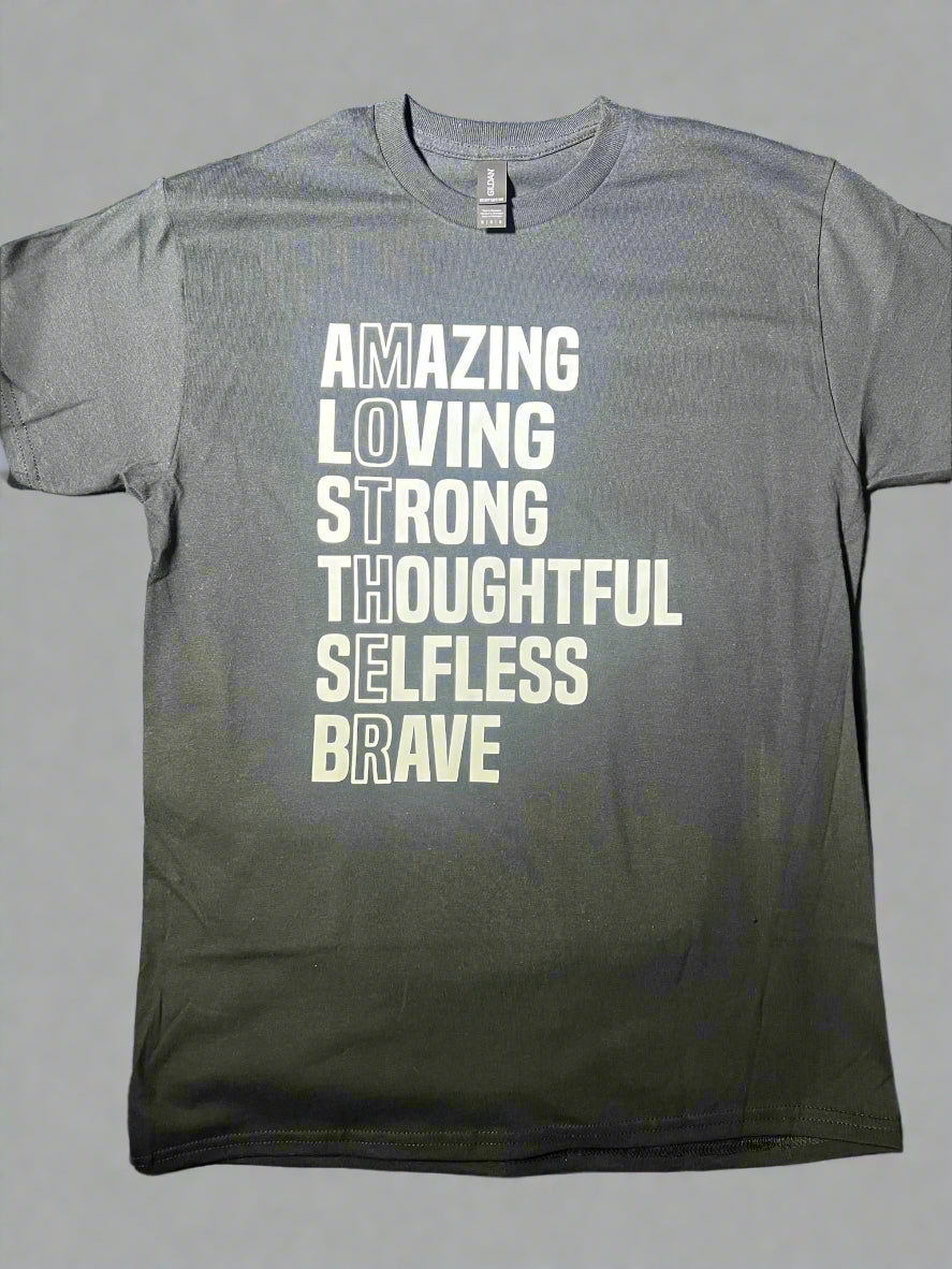A black short-sleeve graphic tee with white text that reads 'AMAZING LOVING STRONG THOUGHTFUL SELFLESS BRAVE' vertically, with the word 'MOTHER' highlighted at the end.