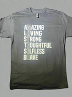 A black short-sleeve graphic tee with white text that reads 'AMAZING LOVING STRONG THOUGHTFUL SELFLESS BRAVE' vertically, with the word 'MOTHER' highlighted at the end.