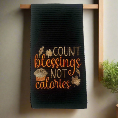 Black embroidered Thanksgiving kitchen towel with Count Blessings Not Calories phrase, muffin, and fall leaves