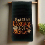 Black embroidered Thanksgiving kitchen towel with Count Blessings Not Calories phrase, muffin, and fall leaves