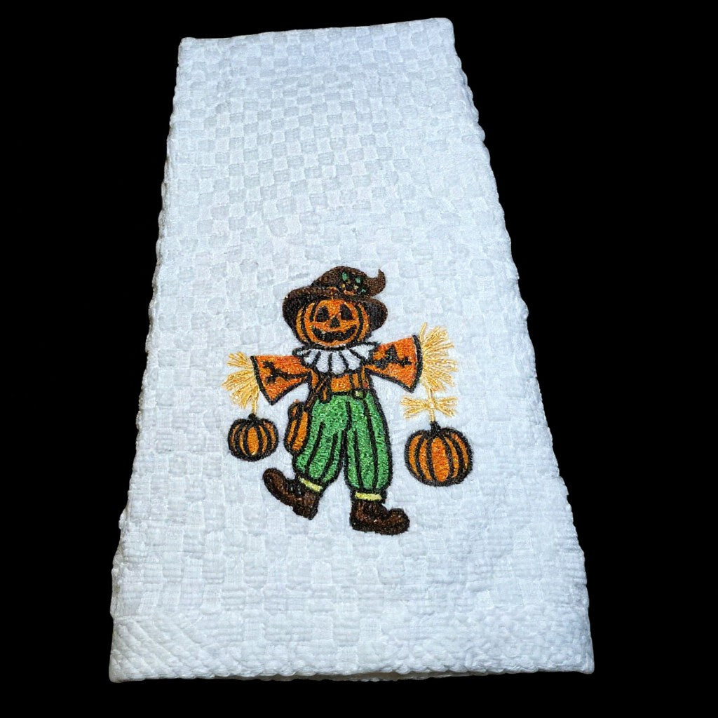 White towel with embroidered scarecrow design on a black background